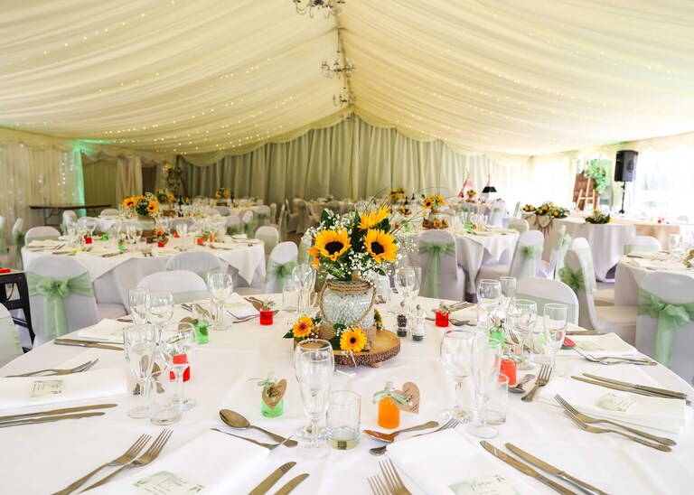 A marquee set up for a wedding breakfast with bright yellow sunflowers at Hungarian Hall on a Wedding Day photographed by Suffolk Wedding Photographers Hayley Denston Photography
