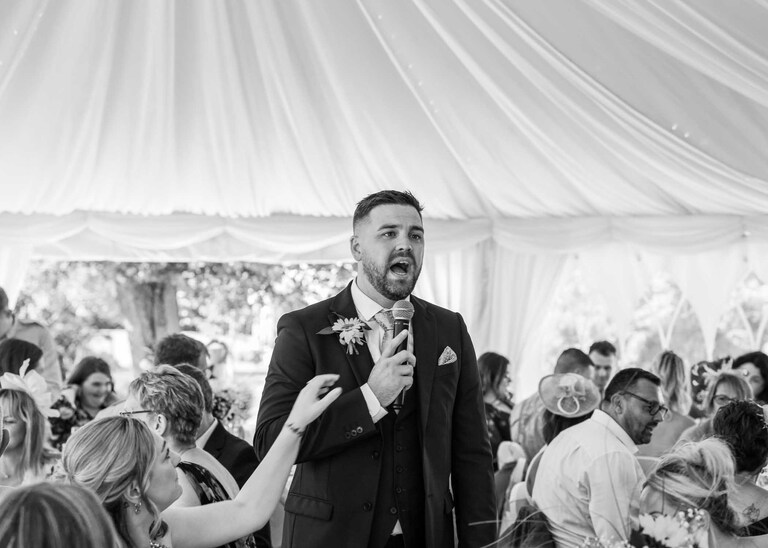 A groomsmen announcing the bride and groom coming in to the marquee for their wedding breakfast at Hungarian Hall on a Wedding Day photographed by Suffolk Wedding Photographers Hayley Denston Photography