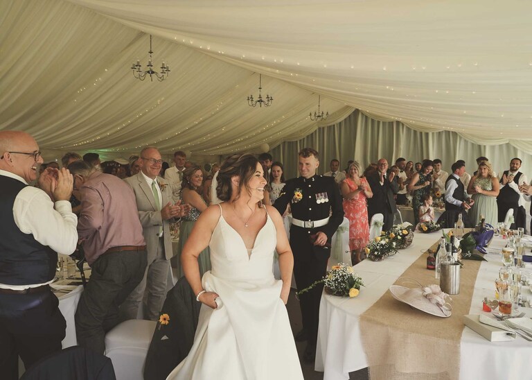 A bride and groom entering the marquee and their wedding breakfast walking to the top table at Hungarian Hall on a Wedding Day photographed by Suffolk Wedding Photographers Hayley Denston Photography