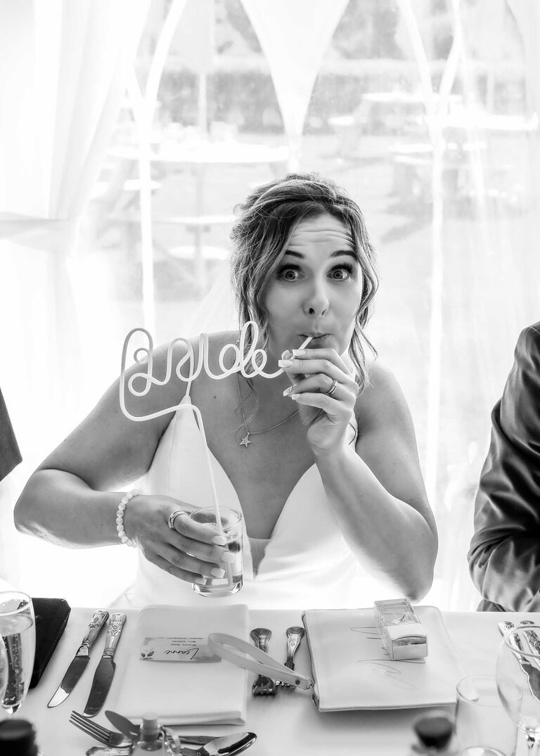 A bride sucking her drink through a brides straw at her wedding breakfast at Hungarian Hall on a Wedding Day photographed by Suffolk Wedding Photographers Hayley Denston Photography