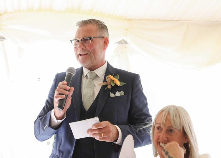 A father of the bride giving his speech whilst the mother of the bride listens at Hungarian Hall on a Wedding Day photographed by Suffolk Wedding Photographers Hayley Denston Photography