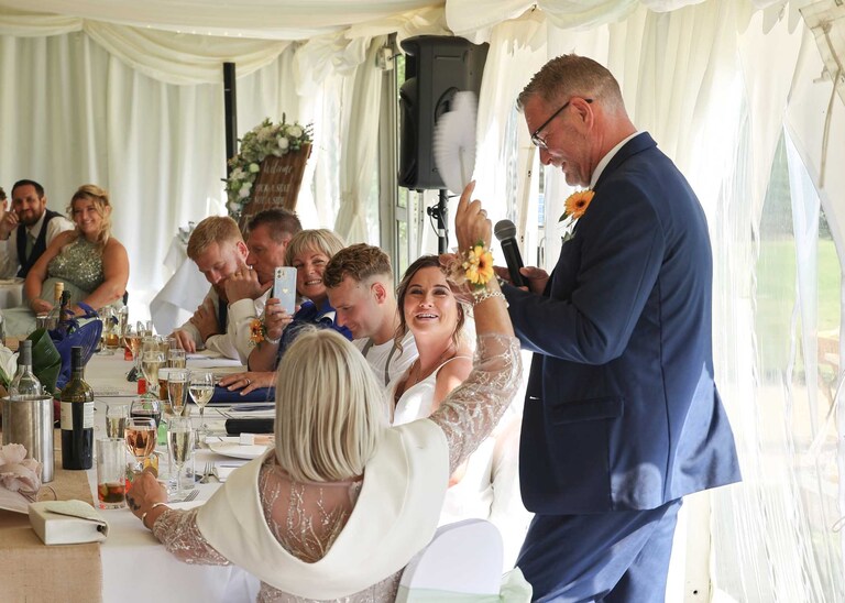 A father of the bride giving his speech whilst being fanned by the mother of the bride at Hungarian Hall on a Wedding Day photographed by Suffolk Wedding Photographers Hayley Denston Photography