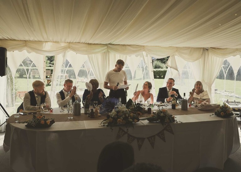 A groom giving his speech at the top table at Hungarian Hall on a Wedding Day photographed by Suffolk Wedding Photographers Hayley Denston Photography
