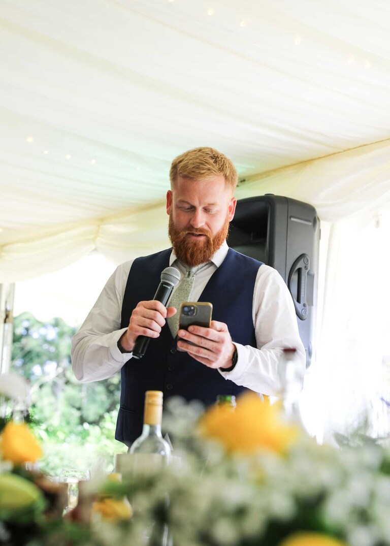 A bestman giving his speech from his phone at Hungarian Hall on a Wedding Day photographed by Suffolk Wedding Photographers Hayley Denston Photography