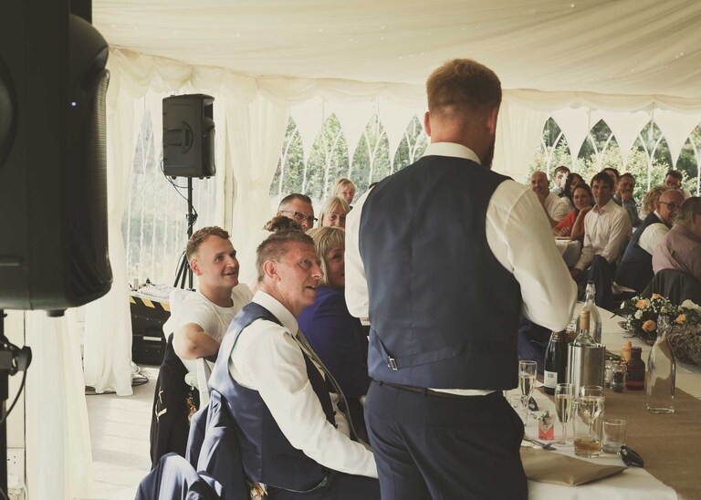 A bestman giving his speech whilst the groom and guests watch on at Hungarian Hall on a Wedding Day photographed by Suffolk Wedding Photographers Hayley Denston Photography