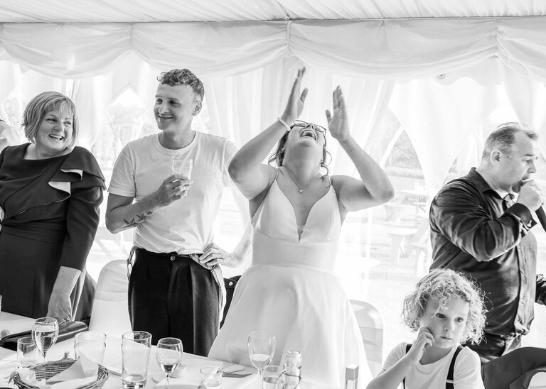 A bride and groom laughing during a singing waiters performance at Hungarian Hall on a Wedding Day photographed by Suffolk Wedding Photographers Hayley Denston Photography