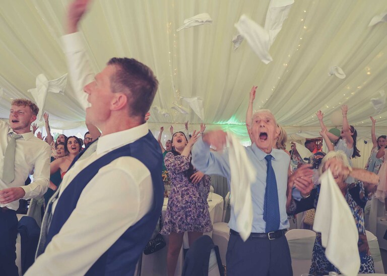 Guests throwing their napkins in the air during a singing waiters performance at Hungarian Hall on a Wedding Day photographed by Suffolk Wedding Photographers Hayley Denston Photography