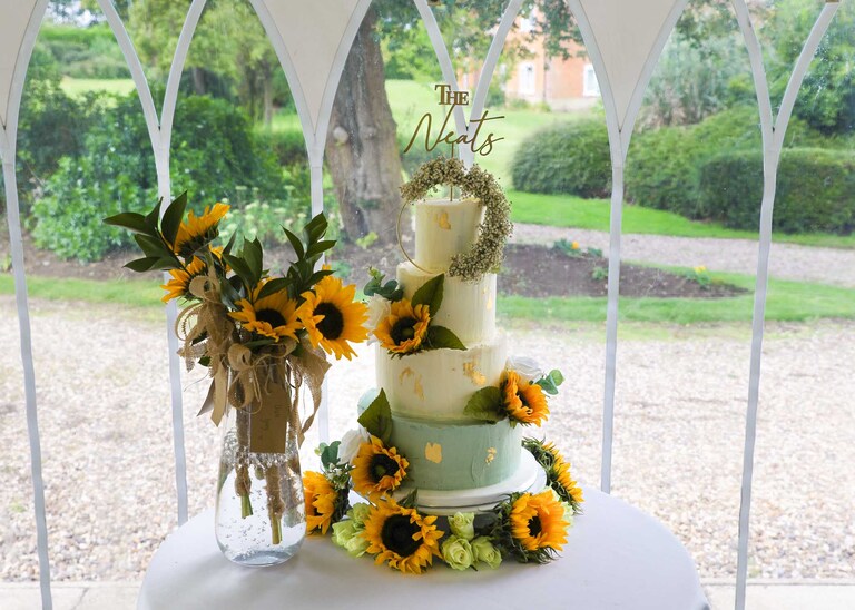 A wedding cake with rustic icing and sunflowers at Hungarian Hall on a Wedding Day photographed by Suffolk Wedding Photographers Hayley Denston Photography