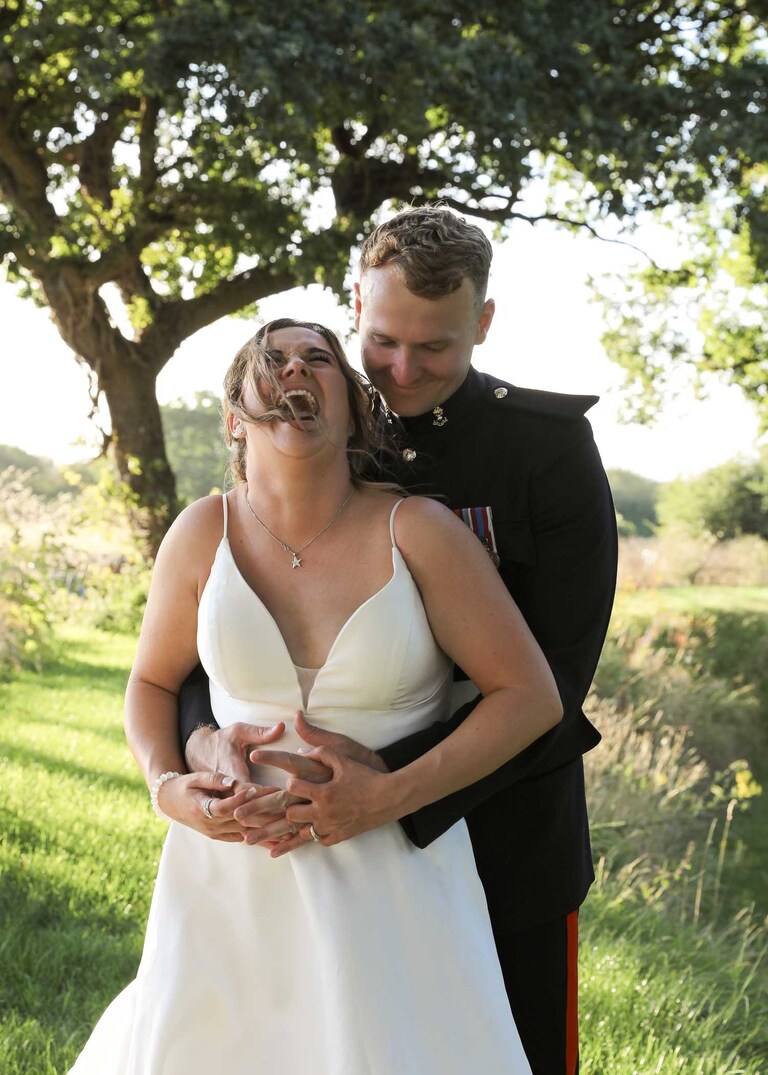 A bride laughing whilst her groom cuddles her at Hungarian Hall on a Wedding Day photographed by Suffolk Wedding Photographers Hayley Denston Photography