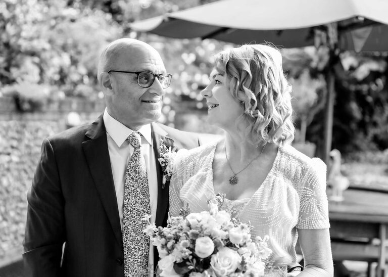 A black and white photo of a bride and groom looking at each other on a rainy wedding day at Letheringham Water Mill by Suffolk Wedding Photographers Hayley Denston Photography
