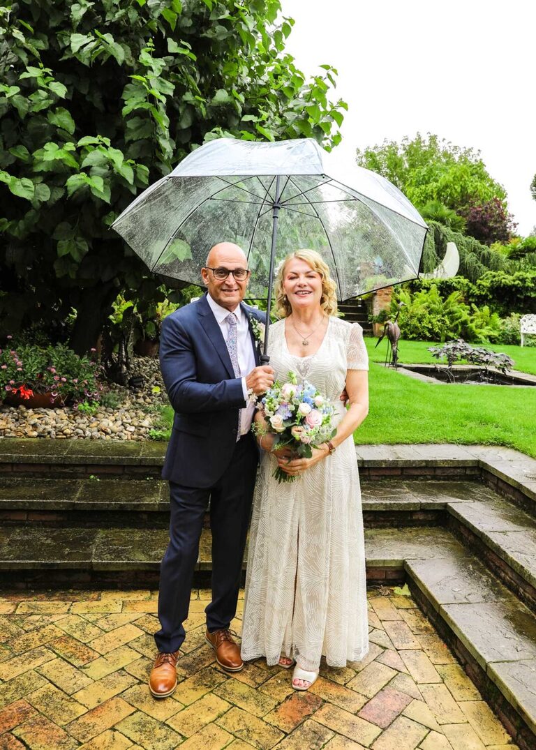 A bride and groom under a clear umbrella on a rainy wedding day at Letheringham Water Mill by Suffolk Wedding Photographers Hayley Denston Photography