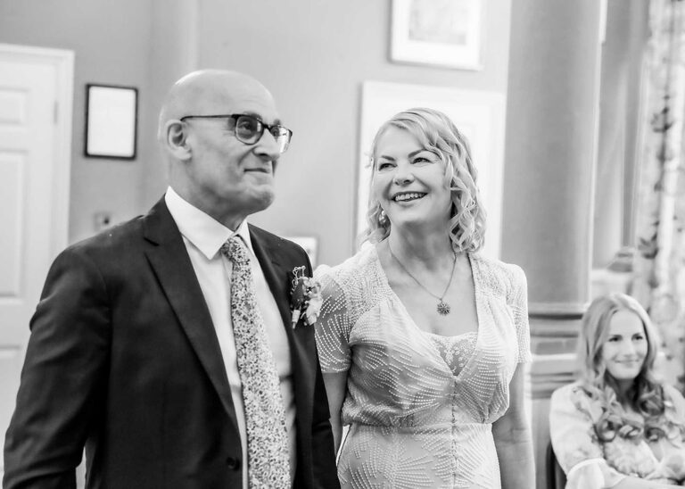A bride looking and smiling at her groom at a wedding ceremony at Woodbridge Shire Hall photographed by Suffolk Wedding Photographers Hayley Denston Photography