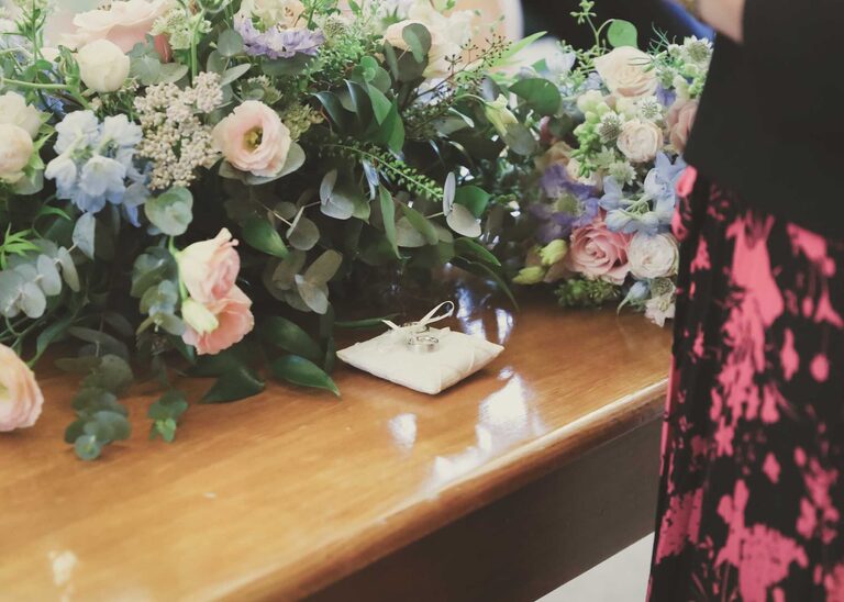 The wedding rings on a little white silk cushion at a wedding ceremony at Woodbridge Shire Hall photographed by Suffolk Wedding Photographers Hayley Denston Photography