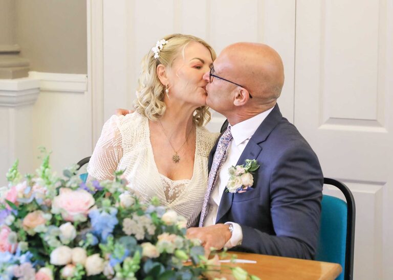 A bride and groom kissing after signing the register on a rainy wedding day at Woodbridge Shire Hall photographed by Suffolk Wedding Photographers Hayley Denston Photography