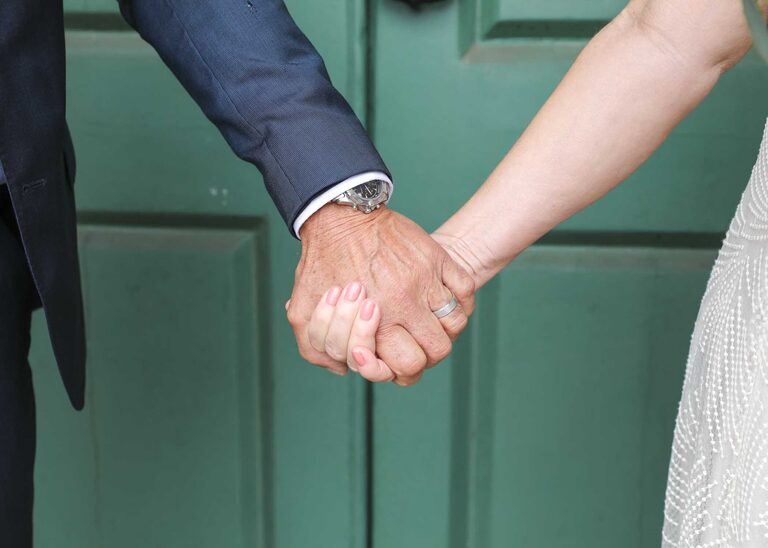 A bride and groom holding hands in front of the green doors on a rainy wedding day at Woodbridge Shire Hall photographed by Suffolk Wedding Photographers Hayley Denston Photography