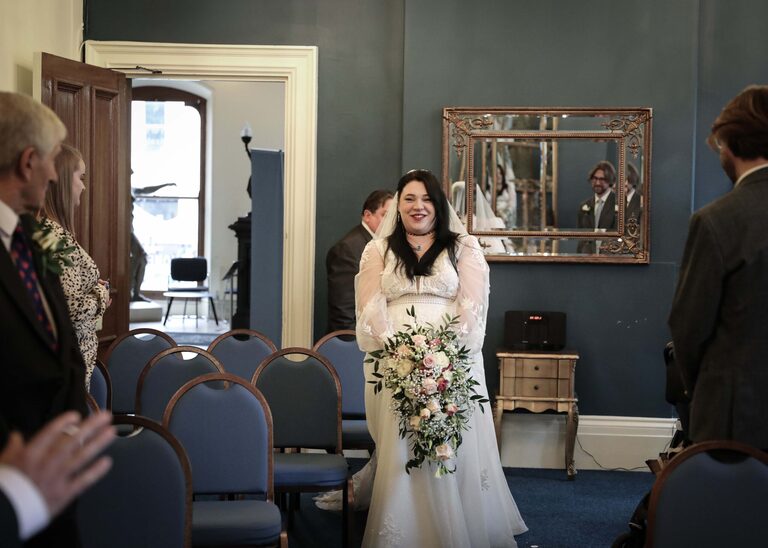 A bride walking up the aisle in the ceremony roomat Ipswich Town Hall taken by Suffolk Wedding Photographer Hayley Denston Photography