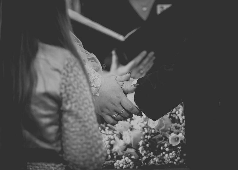 A black and white photo of a bride and groom holding hands during their wedding ceremony at Ipswich Town Hall taken by Suffolk Wedding Photographer Hayley Denston Photography