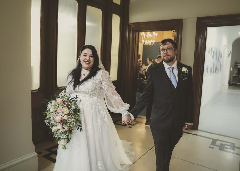 A bride and groom holding hands and walking out of their wedding ceremony at Ipswich Town Hall taken by Suffolk Wedding Photographer Hayley Denston Photography
