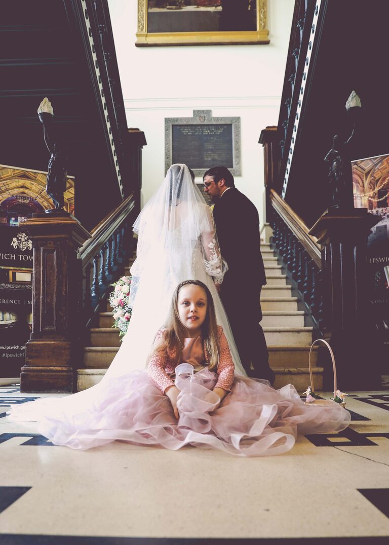 A flowergirl sat on her mum's wedding dress train at Ipswich Town Hall taken by Suffolk Wedding Photographer Hayley Denston Photography