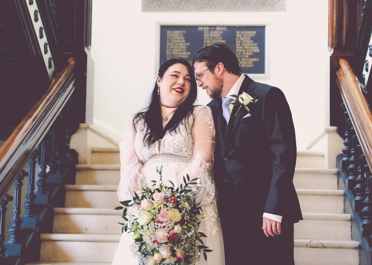 A bride and groom looking at each other and smiling on the stairs on their wedding day at Ipswich Town Hall taken by Suffolk Wedding Photographer Hayley Denston Photography