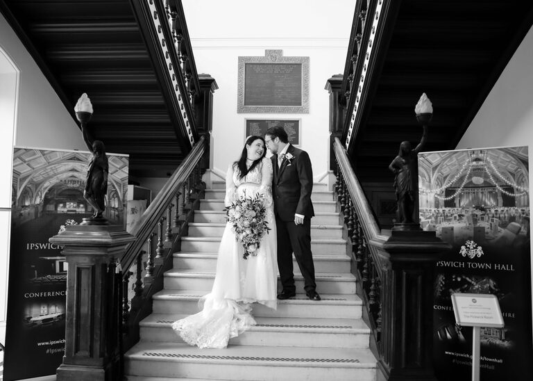 A black and white photo of a bride and groom on the stairs on their wedding day at Ipswich Town Hall taken by Suffolk Wedding Photographer Hayley Denston Photography
