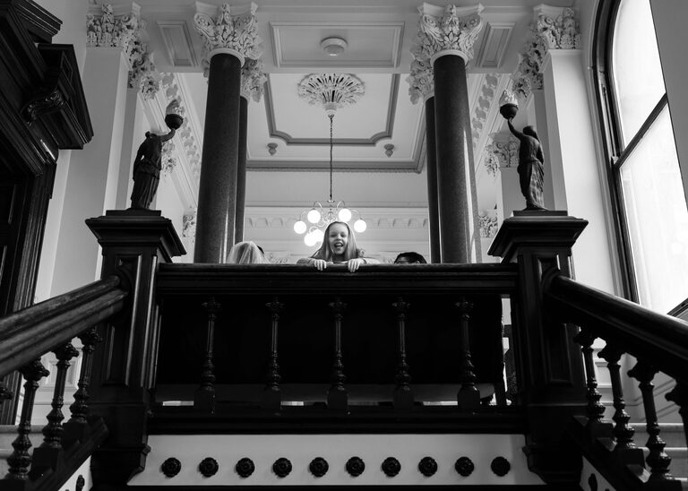 A flowergirl peeping over the stairs at Ipswich Town Hall taken by Suffolk Wedding Photographer Hayley Denston Photography