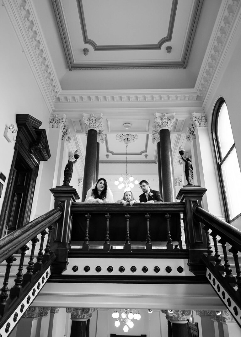 A bride, groom and a flowergirl all looking down the stairs at Ipswich Town Hall taken by Suffolk Wedding Photographer Hayley Denston Photography