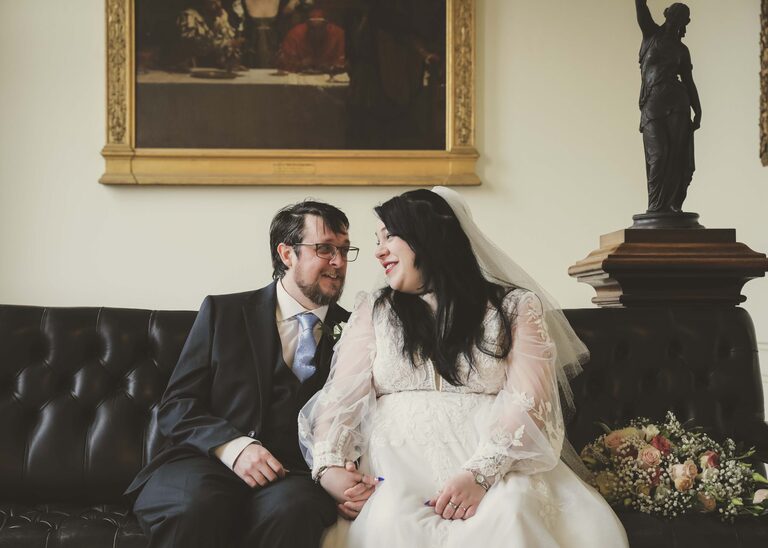 A bride and groom looking at each other on their wedding day sat on a leather sofa at Ipswich Town Hall taken by Suffolk Wedding Photographer Hayley Denston Photography