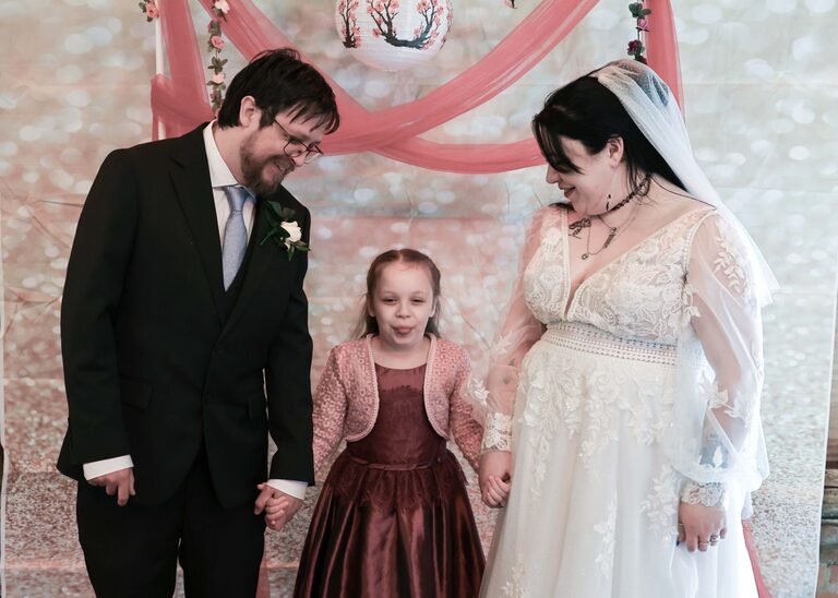 A bride and groom with their daughter in the middle at the Tithe Barn Sproughton on a wedding day taken by Suffolk Wedding Photographer Hayley Denston Photography