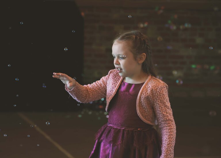 A flowergirl playing with touchable bubbles on a wedding day at the Tithe Barn Sproughton on a wedding day taken by Suffolk Wedding Photographer Hayley Denston Photography