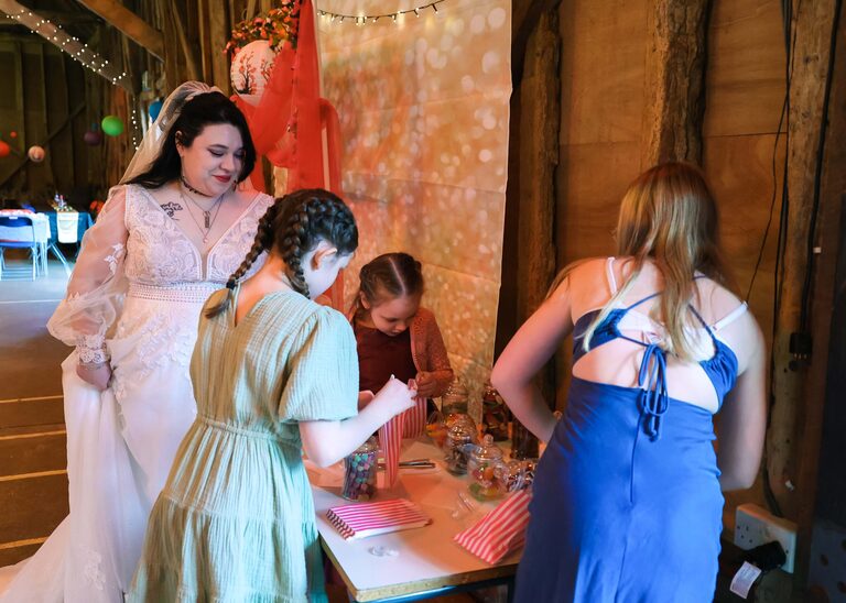 A bride watching children choosing sweets from a pick n mix on a wedding day at the Tithe Barn Sproughton on a wedding day taken by Suffolk Wedding Photographer Hayley Denston Photography
