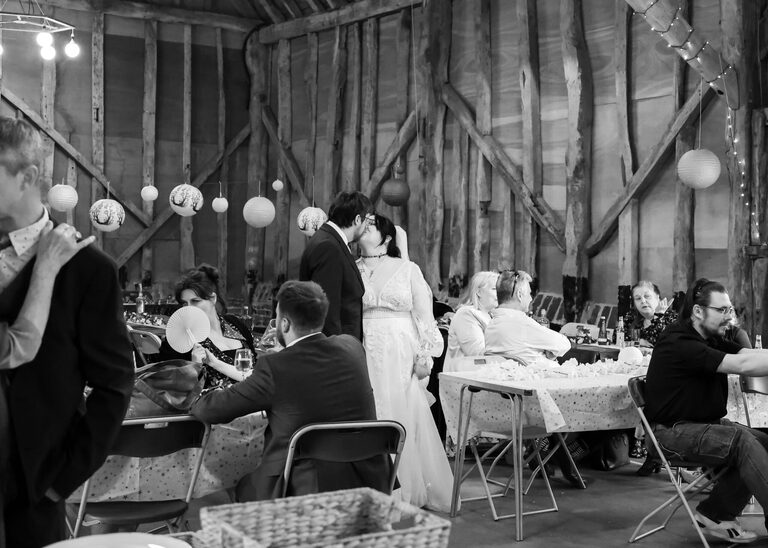 A bride and groom stood in the middle of a barn kissing on their wedding day at the Tithe Barn Sproughton on a wedding day taken by Suffolk Wedding Photographer Hayley Denston Photography