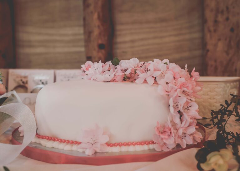 A simple one layer wedding cake decorated with pink cherry blossom flowers at the Tithe Barn Sproughton on a wedding day taken by Suffolk Wedding Photographer Hayley Denston Photography