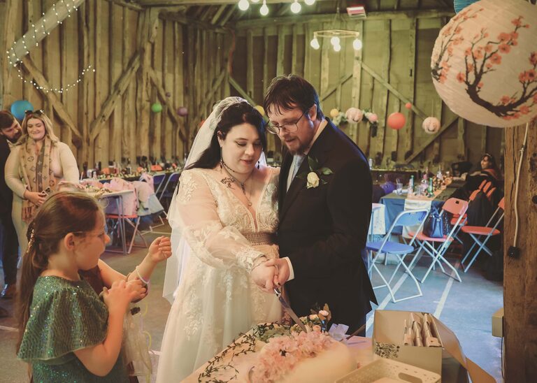 A bride and groom cutting their wedding cake at the Tithe Barn Sproughton on a wedding day taken by Suffolk Wedding Photographer Hayley Denston Photography