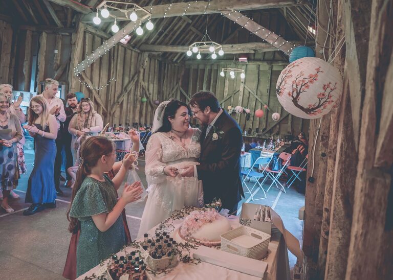 A bride and groom cutting their wedding cake at the Tithe Barn Sproughton on a wedding day taken by Suffolk Wedding Photographer Hayley Denston Photography