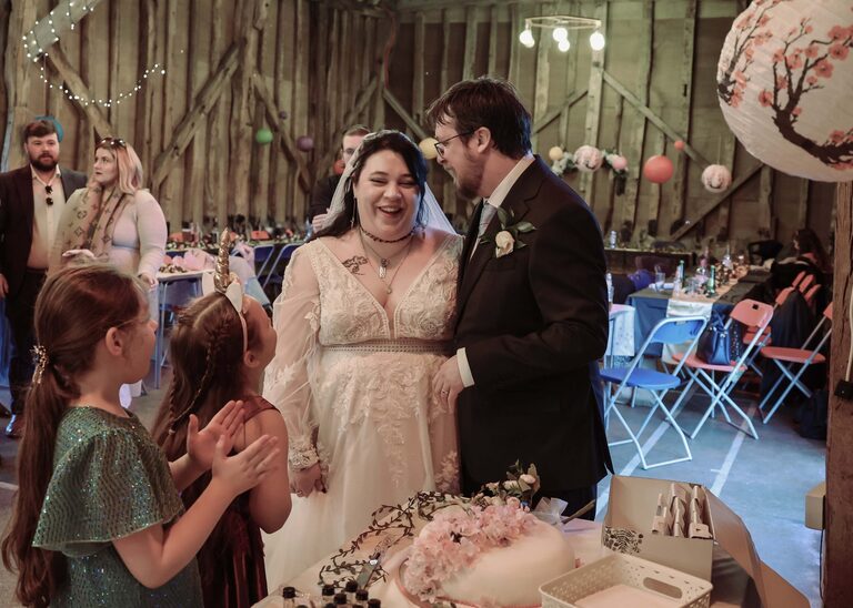 A bride and groom laughing together after cutting their wedding cake at the Tithe Barn Sproughton on a wedding day taken by Suffolk Wedding Photographer Hayley Denston Photography