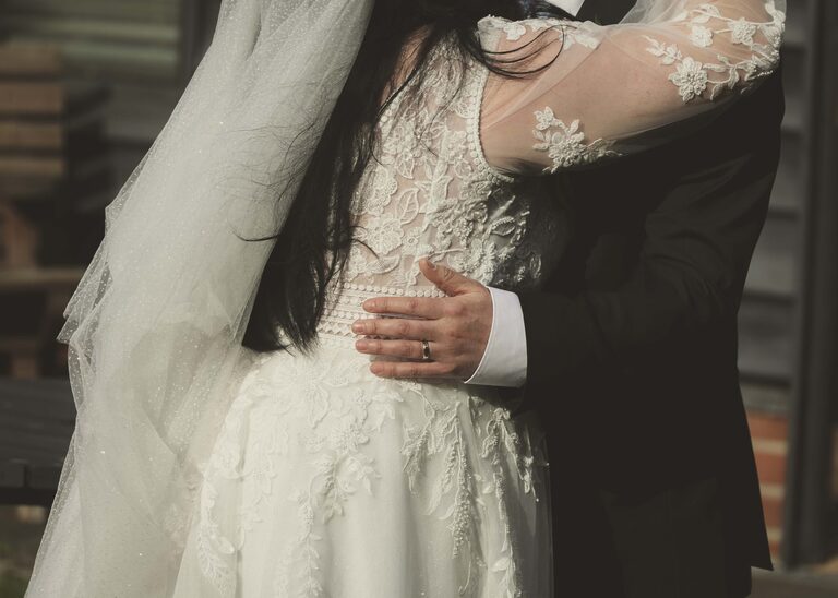 A grooms arms hugging his bride on their wedding day at the Tithe Barn Sproughton on a wedding day taken by Suffolk Wedding Photographer Hayley Denston Photography