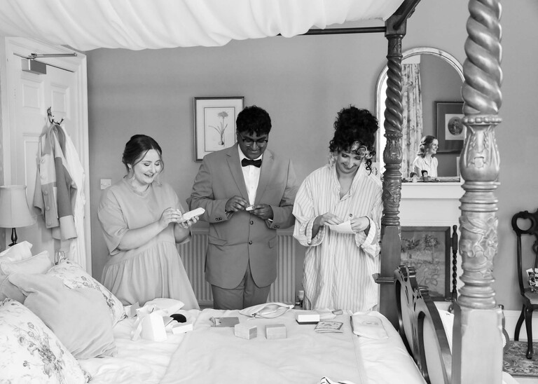 A black and white photo of bridesmaids and bridesman receiving presents from the bride on a wedding day at Bressingham Hall and High Barn captured by Suffolk Wedding Photographers Hayley Denston Photography