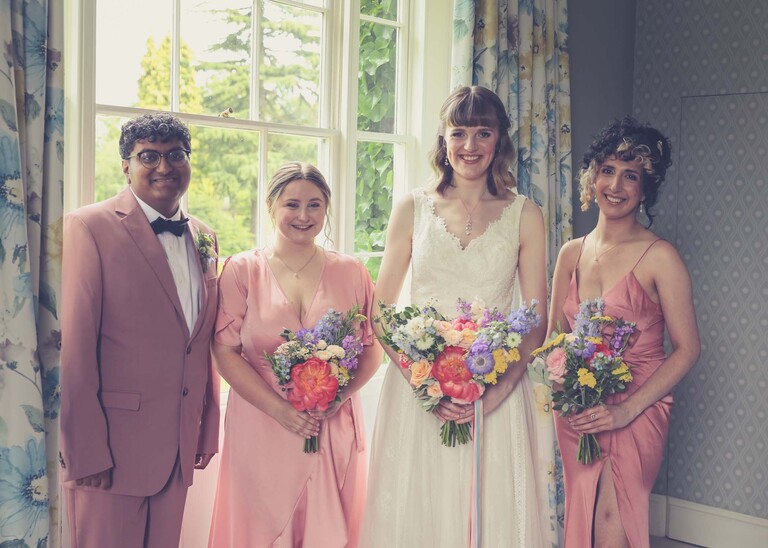 A bride, her bridesmaids and a bridesman stood in front of a sash window on a wedding day at Bressingham Hall and High Barn captured by Suffolk Wedding Photographers Hayley Denston Photography