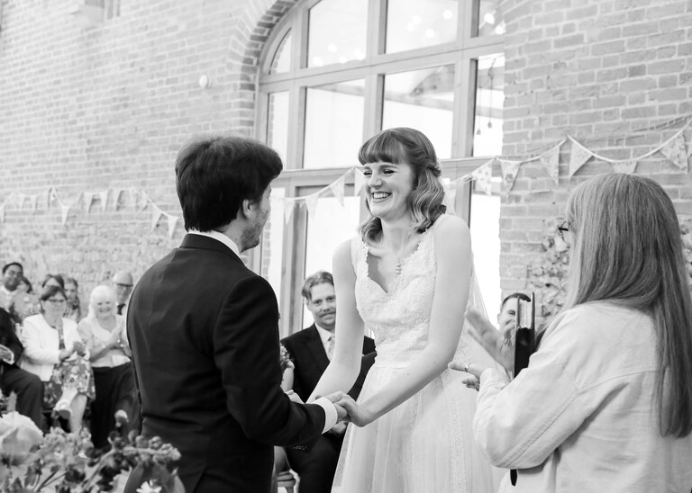 A bride and groom at their wedding ceremony in a large barn on a wedding day at Bressingham Hall and High Barn captured by Suffolk Wedding Photographers Hayley Denston Photography