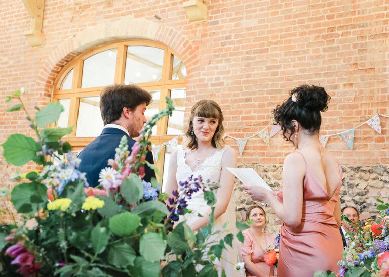 A bride and groom at their wedding ceremony in a large barn on a wedding day at Bressingham Hall and High Barn captured by Suffolk Wedding Photographers Hayley Denston Photography