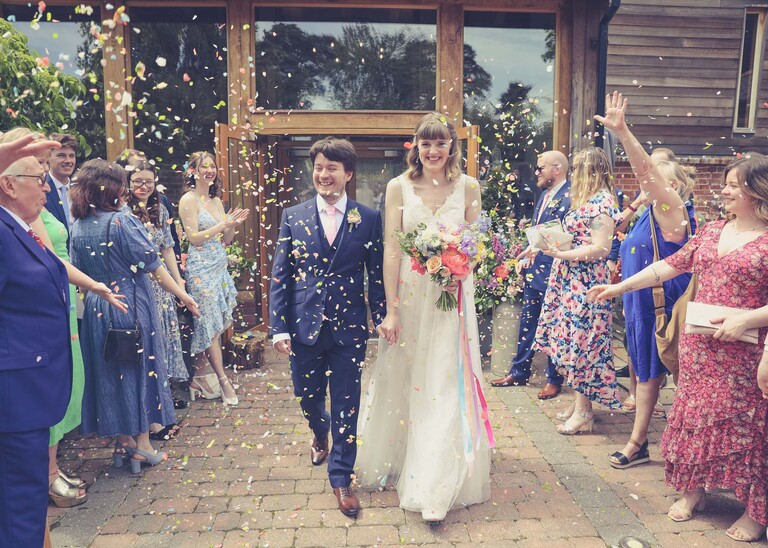A bride and groom walking through a confetti aisle on a wedding day at Bressingham Hall and High Barn captured by Suffolk Wedding Photographers Hayley Denston Photography