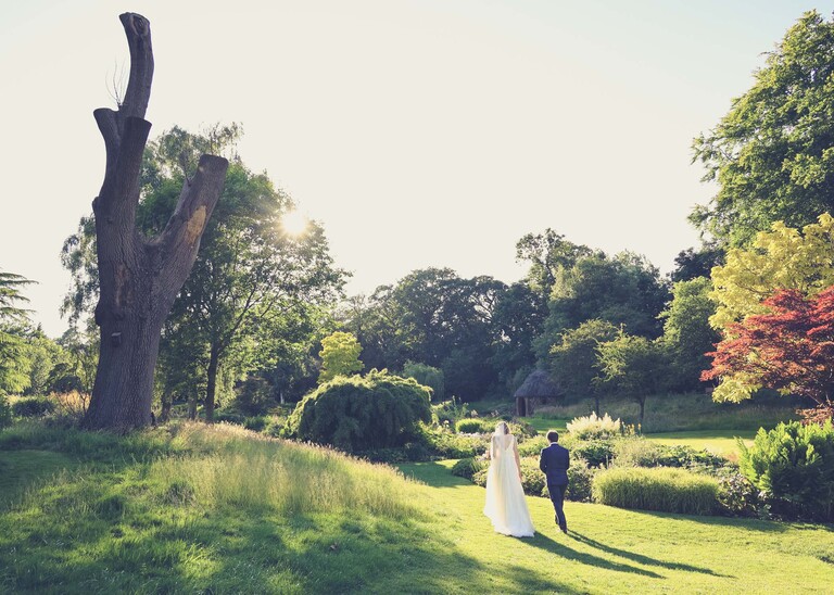 A bride and groom walking through Bressingham Gardens in golden hour on a wedding day at Bressingham Hall and High Barn captured by Suffolk Wedding Photographers Hayley Denston Photography