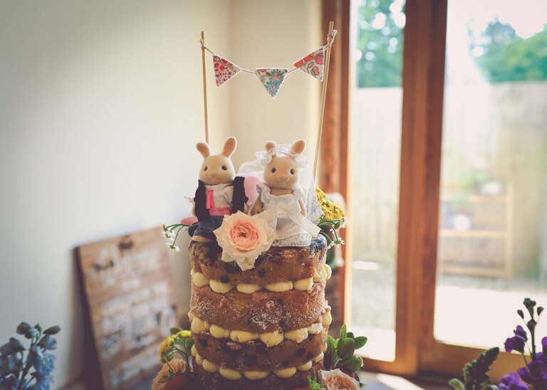 A beautiful naked victoria sponge wedding cake with sylvalian family cake toppers on a wedding day at Bressingham Hall and High Barn captured by Suffolk Wedding Photographers Hayley Denston Photography