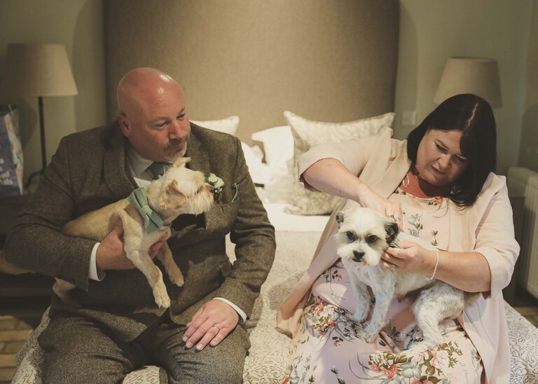 A brides parents putting two little bow ties of their dogs on a wedding day at Easton Grange captured by Suffolk Wedding Photographers Hayley Denston Photography
