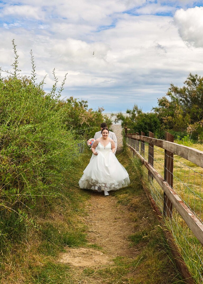 A bride hitching up her dress and walking back to her wedding venue after a trip to the beach wedding day at Thorpeness Country Club captured by Suffolk Wedding Photographers Hayley Denston Photography