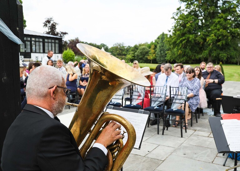 A Tuba player playing to a wedding ceremony on a wedding day at Swynford Manor in Suffolk Captured by Suffolk Wedding Photographer Hayley Denston Photography