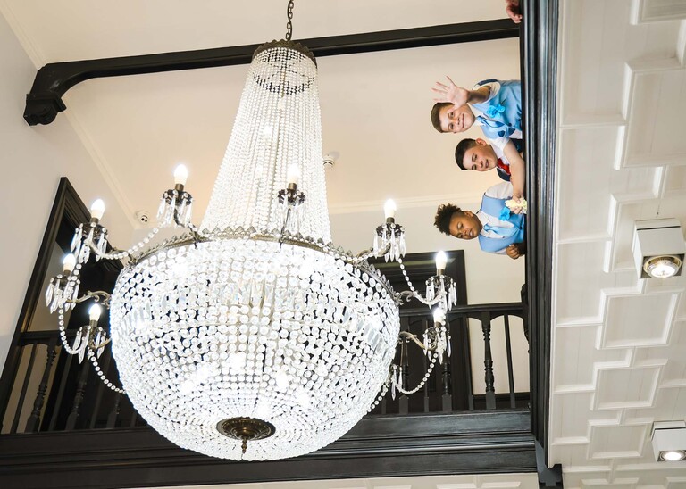 Children looking over a balcony with her chandelier waiting for confetti on a wedding day at Swynford Manor in Suffolk Captured by Suffolk Wedding Photographer Hayley Denston Photography