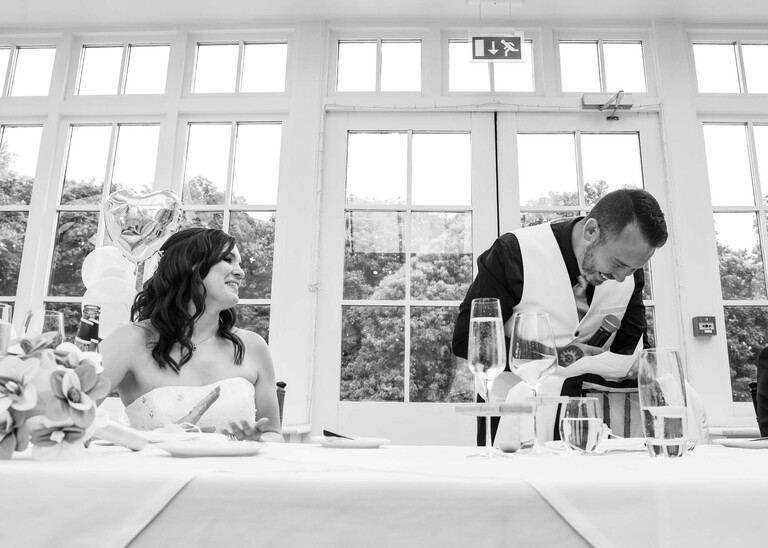 A black and white photo of the groom laughing at himself during speeches on a wedding day at Swynford Manor in Suffolk Captured by Suffolk Wedding Photographer Hayley Denston Photography 