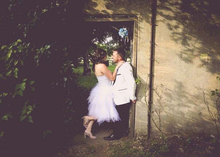 A bride leaning in to her groom in an archway of a brick wall on a wedding day at Swynford Manor in Suffolk Captured by Suffolk Wedding Photographer Hayley Denston Photography